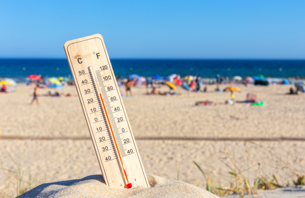 beach scene with thermometer stuck in sand showing high heat