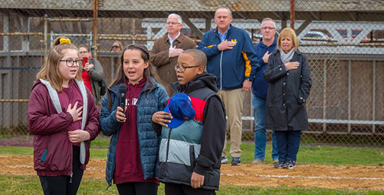 Three children standing with hands over their hand over their heart as they sing the National Anthem before the game.