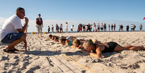 participants lay on the sand as the coach prepares to blow the whistle starting the next training drill