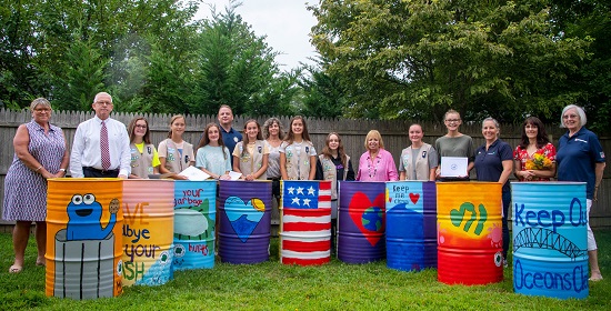 Supervisor Carpenter DPW Commisioner Tom Owens Girl Scout representatives stand beside the girl scouts behind the cans they painted with colorful pictures and murals on them.