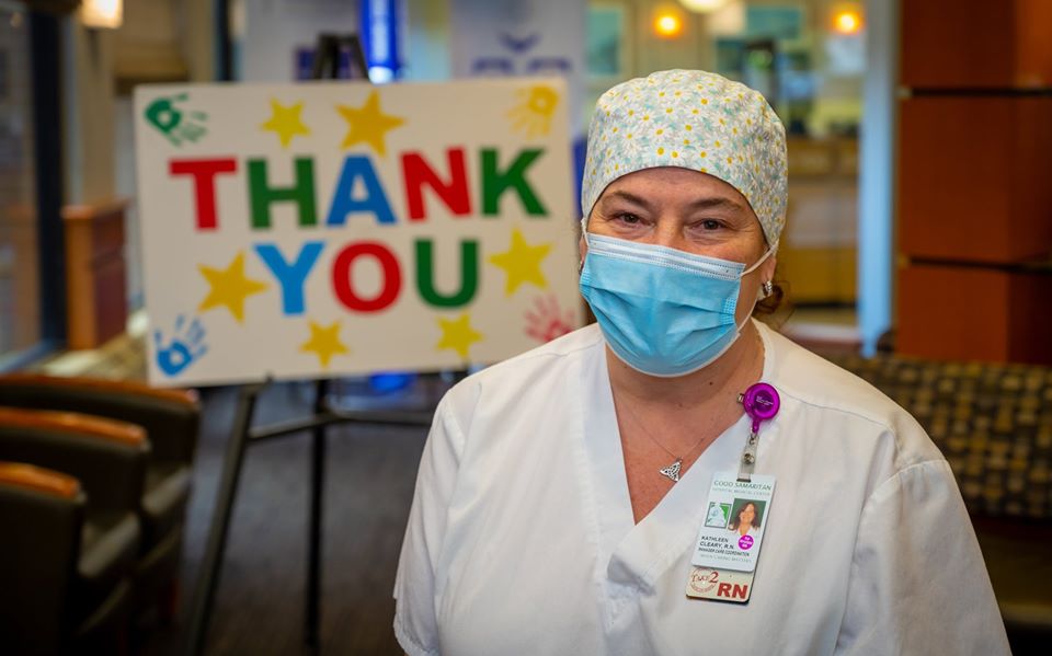 A closeup of a nurse in PPE with a thank you sign behind her