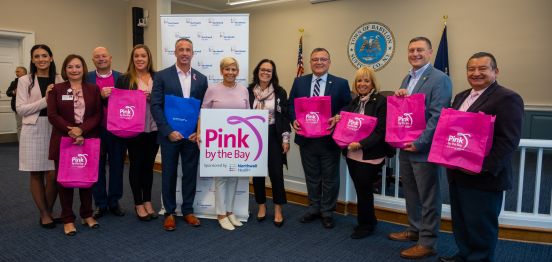 group shot with pink by hte bay sign