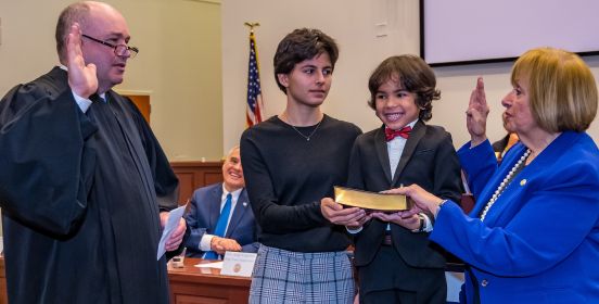 Supervisor Carpenter raising her right hand during swearing in, accompanied by grandaughter and grandson.