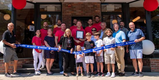 group with ribbon in front of pizzeria