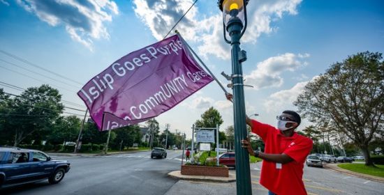 man hangs Islip Goes Purple sign from light post