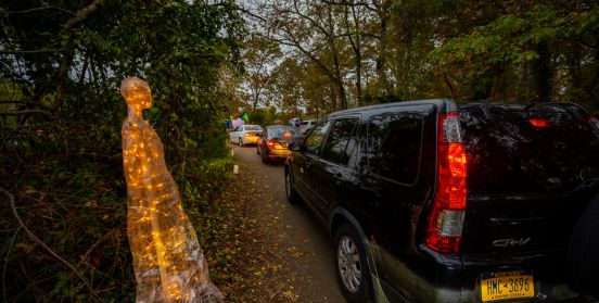 cars in a row, lining up to enter movie, as ghostly decorations greet them