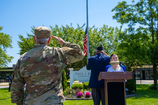 A man in army fatigues salutes the flag at half mast