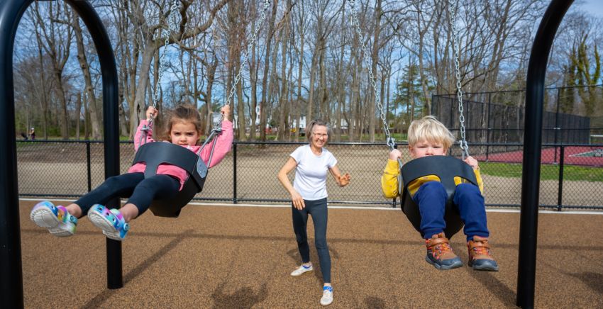 A woman pushes 2 children on new swings