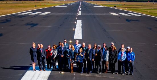 Supervisor Carpenter, Councilman Cochrane, Councilwoman Mullen and members of ISP staff stand on the new runway as a high up shot takes a picture below, the new runway narrowing into the vanishing point behind them.