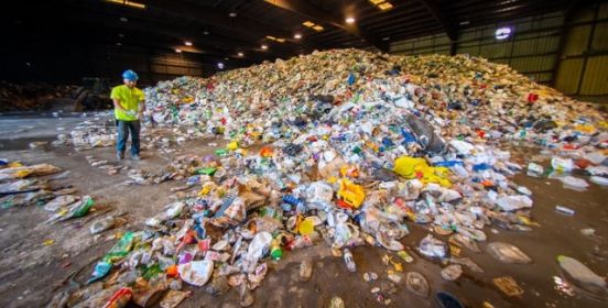 Sanitation worker standing in a facility, surrounded by piles of refuse.