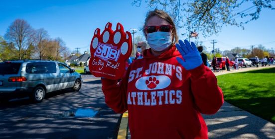 lady in st. john baptist hoodie, fanfare and ppe waves to camera