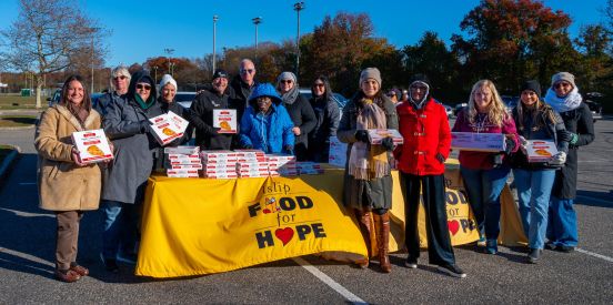 Volunteers hold up boxes infront of Islip Food For Hope table with logo
