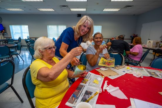 Seniors work on crafts as instructor leans over to provide guidance