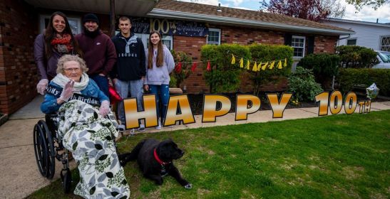 Ehtel, her dog, and her family all pose for a group photo with happy 100 written across her lawn