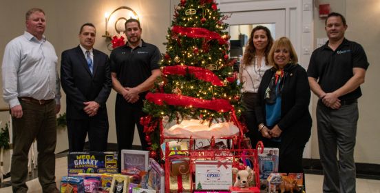 Supervisor Carpenter, Youth Bureau Executive Director Tim Mare and representatives from UPSEU pose for a photo beside the Town Hall Rotunda Tree with toys spilling from under its brances.