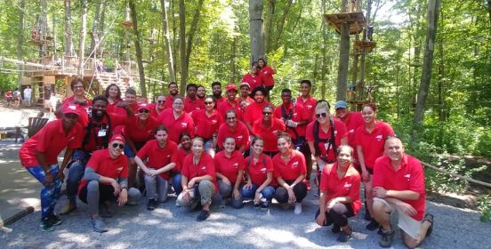 YES emloyees form up, some kneeling, hunching, or standing for a large group photo in front of a playground surrounded by sun-bathed trees.