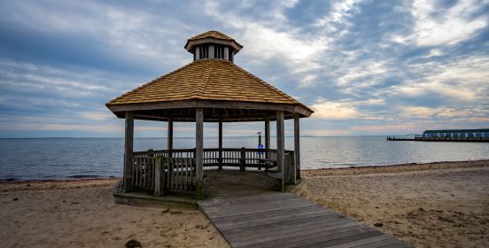 The round new gezbo roof shown in stark relief against the backdrop of silvery smooth shores under a cloud-laden sunset sky.