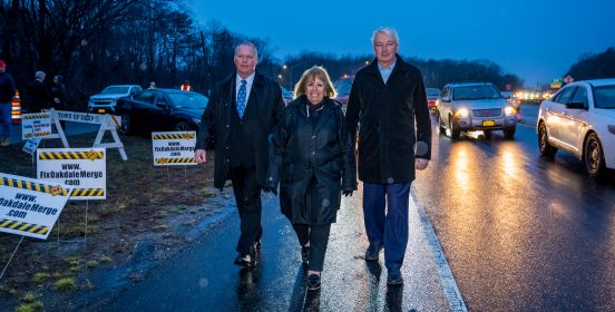 Town Supervisor Carpenter, Marc Herbst of LICA and Senator Phil Boyle walk alongn the traffic heavy Oakdale merge with cars to their left and signs calling for a fix to their right.