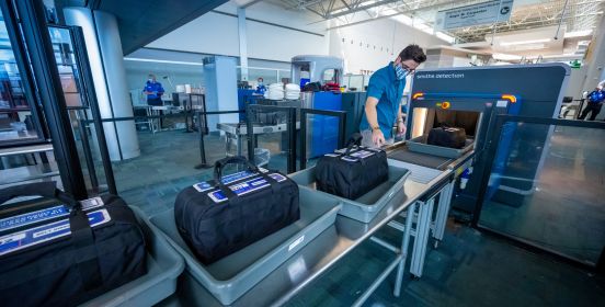 bags wait on conveyor belt for scanner