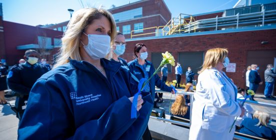 Nurses and medical staff watch ceremony, some holding flowers