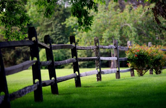 A scenic image of a fence extending from foreground into background with well manicured grass extending throughout