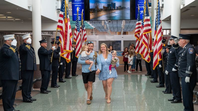 Soldier and family walk down the reception area, flags and servicemembers to their right and left