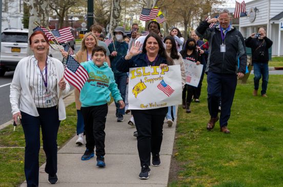 Community walks the sidewalk with signs showing support