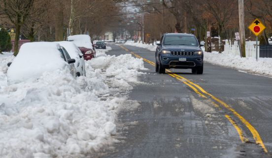 Cars on side of road covered in snow while passing vehicle veers over median to pass safely