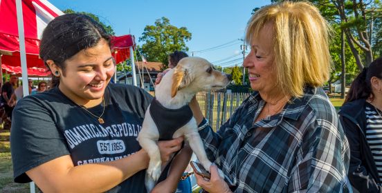 Supervisor Carpenter shakes the paw of a small pooch and its owner as the 2 look on with smiles.