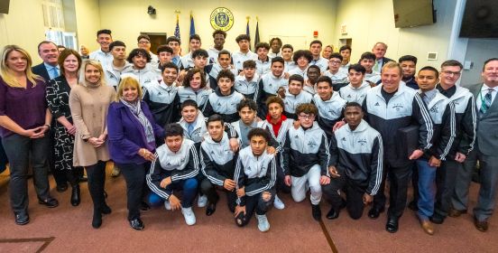 An image of Islip Town Board and Brentwood Boys Soccer Team all squeezed into the Town Board Room for a large group photo.