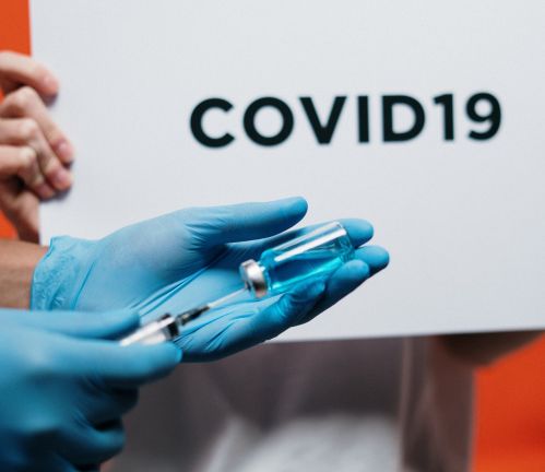 gloved hands drawing vaccine into needle with covid-19 written on sign