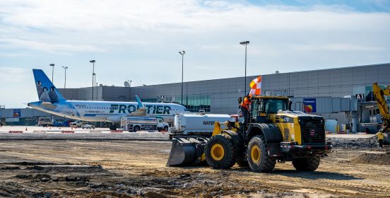 bobcat construction vehicle rides across the work site with plance at terminal in the distance