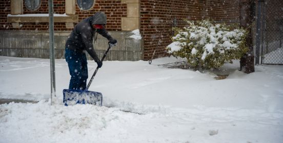 man with shovel clears sidewalk of snow